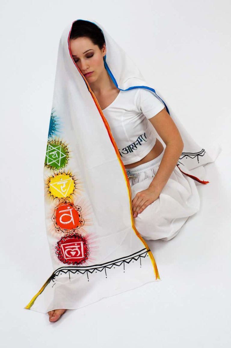 A woman in white practicing kundalini yoga meditation shows what meditation wraps are for by draping one across her head that is painted with brightly coloured chakras.