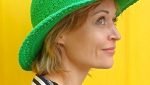 New Yogamasti ambassador Yoga teacher Rebecca Hannah smiling wearing a green sun hat on a yellow background.