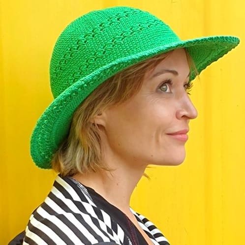 New Yogamasti ambassador Yoga teacher Rebecca Hannah smiling wearing a green sun hat on a yellow background.