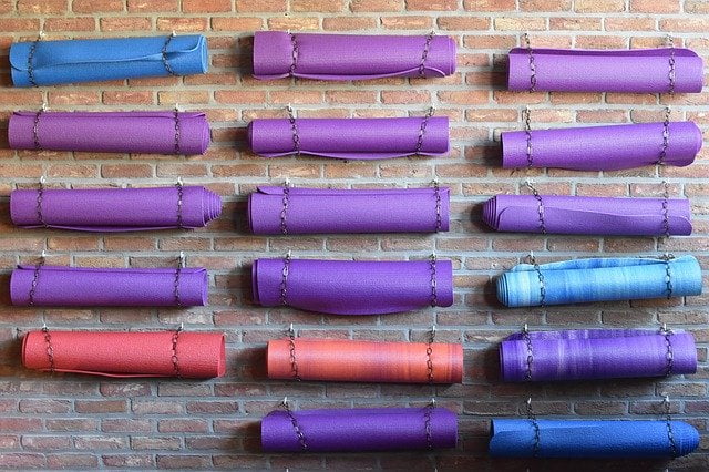 Are Yoga studios open? Yes - if you bring your own mat and clean it religiously! This image shows a studio wall with a variety of colourful Yoga mats hanging up.