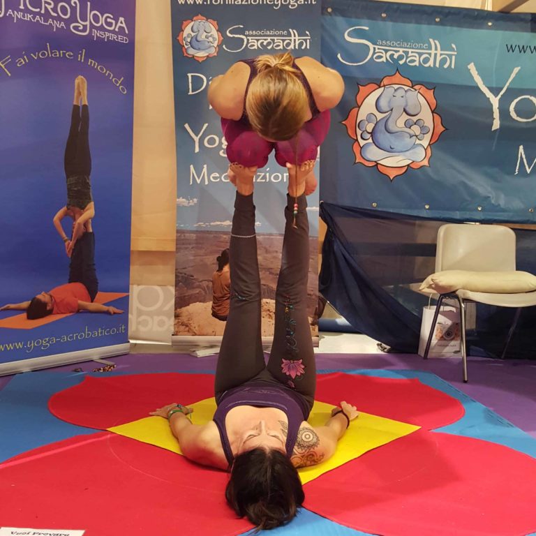 An acroyoga lift with two women. one is raising a kneeling woman into the air using only her leg strength.