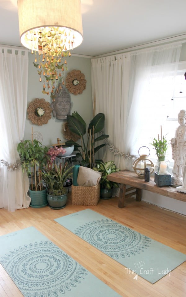 Beautiful yoga room with a buddha mask on the wall and many potted plants in the corner, plus a large chandelier