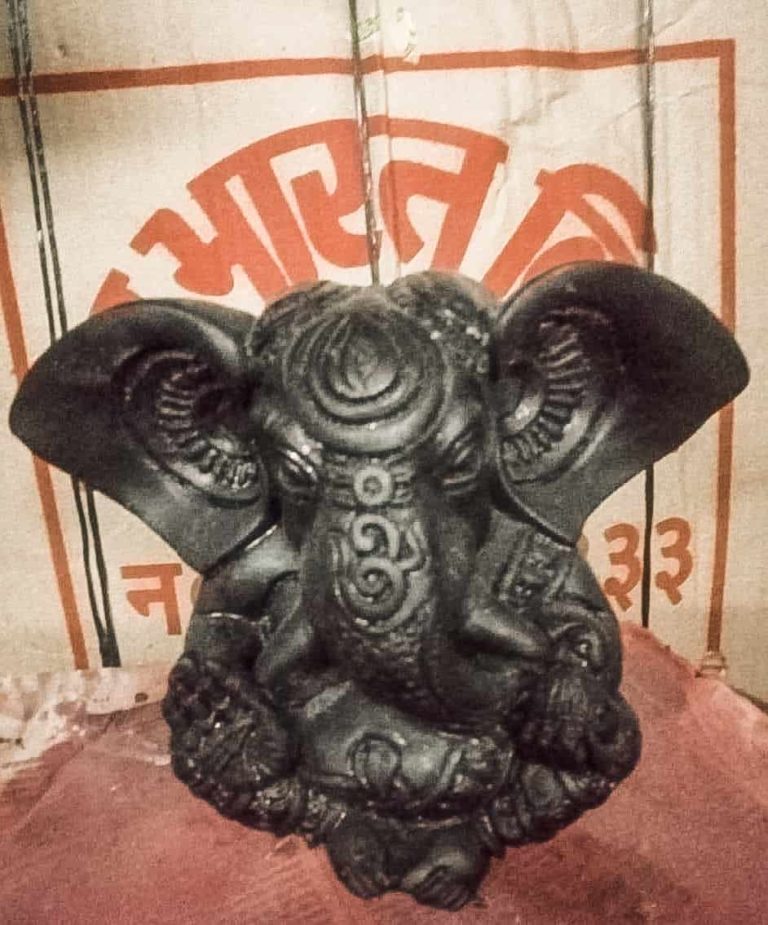 A black clay Ganesha statue with oversized ears and engraved patterns across the body.