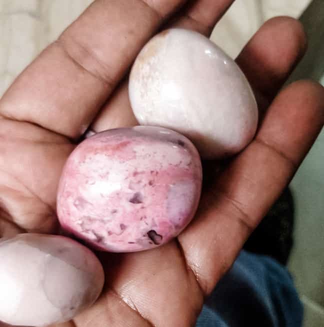 pink egg-sized rhodochrosite crystals laying on the palm of a hand