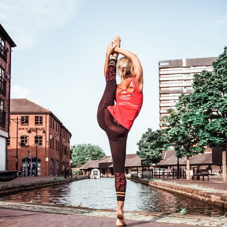 A yoga teacher doing a standing splits yoga pose by the canal in one of our best yoga outfits.
