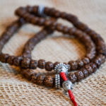 Rudraksh mala beads with silver spacers and a silver buddha head bead hanging from the red cord