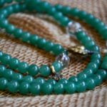 green jade mala beads with faceted quartz spacer beads and decorative metal leaf shaped charms. Close up view.