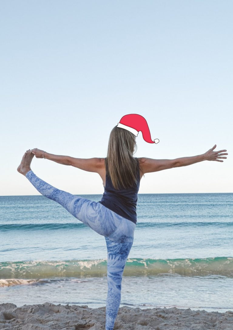  a woman in a santa hat practicing yoga on the beach in blue leggings