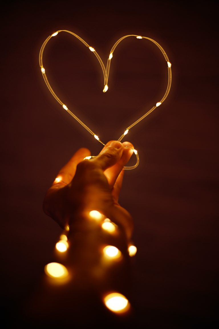 A hand holding fairy lights that have been bent into the shape of a heart