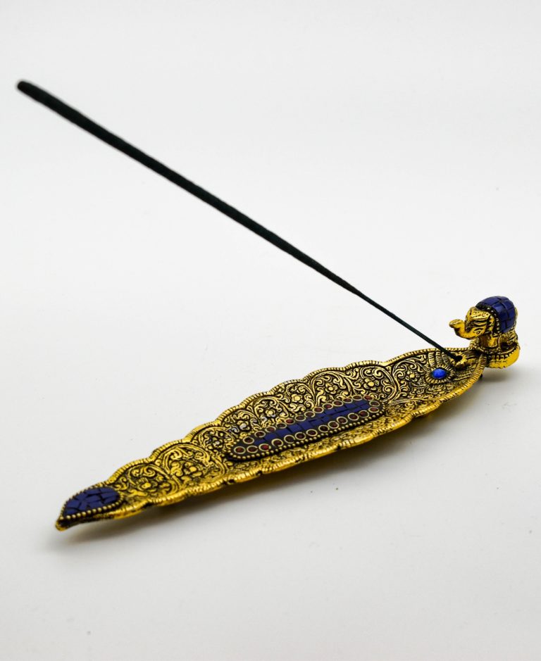 A gold elephant incense holder. It is a leaf shape with engraved patterns and tiny mosaics down the center and on the elephant.