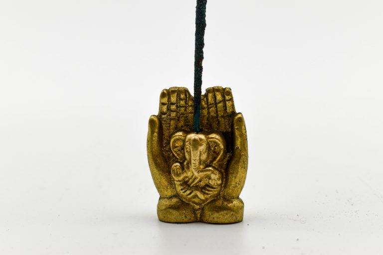 A mini ganesha statue depicted in cupped hands. An incense stick is in a drilled hole on the top of his head.