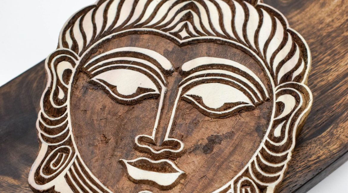 A large buddha head wood block for printing. A carved wooden wood block on a dark wood displayed as spiritual decor.