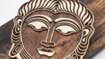A large buddha head wood block for printing. A carved wooden wood block on a dark wood displayed as spiritual decor.