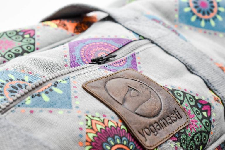 A close up view of a small leather patch with the yogamasti logo, on the top of the extra large mandala yoga mat bag