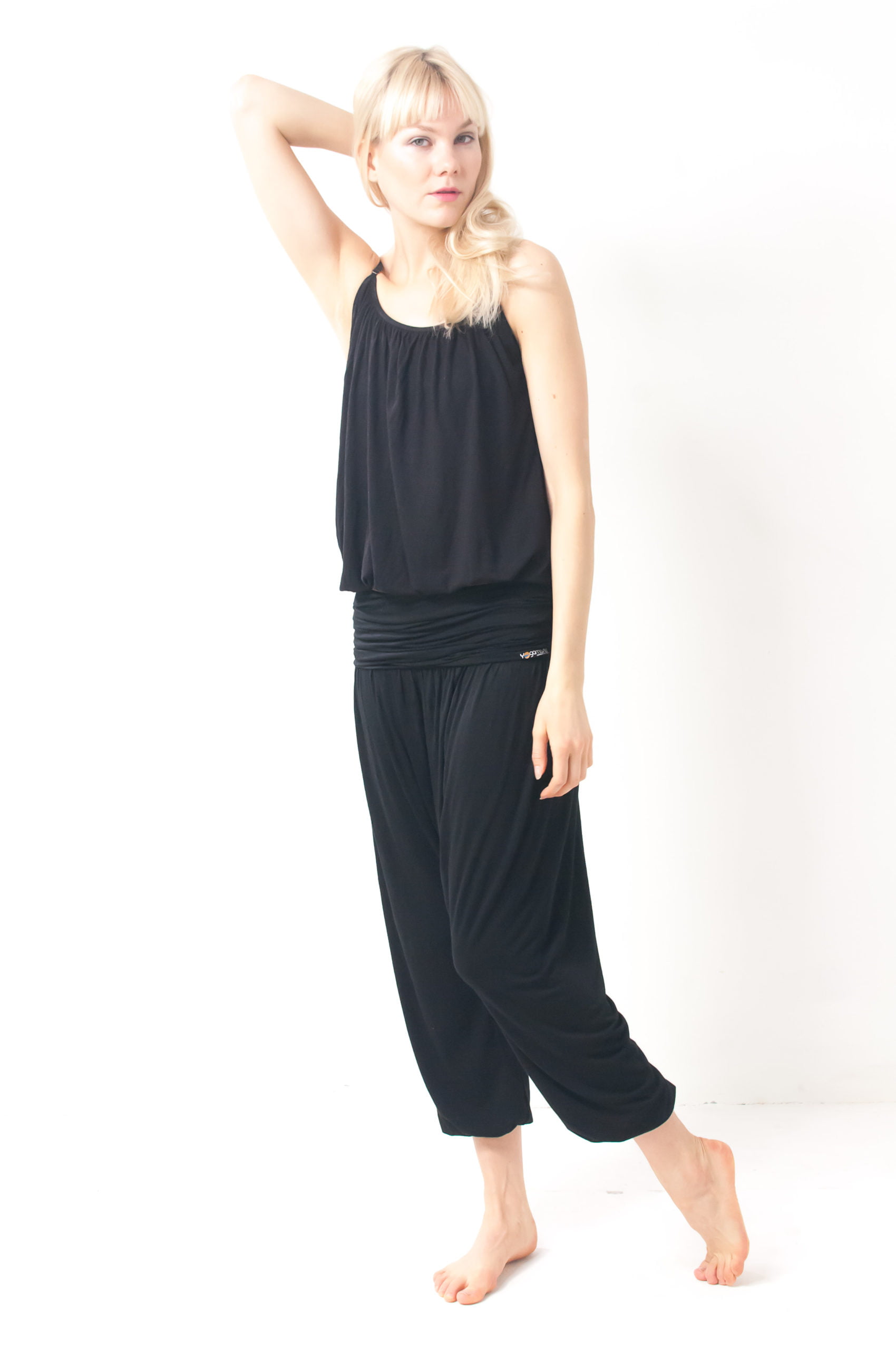 a model wearing black harem yoga pants and a loose black sleeveless top by yogamasti. she is in a relaxed pose with an arm behind her head