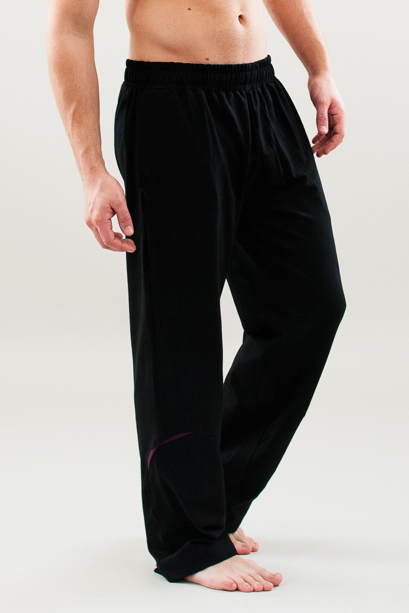 Black yoga pants for men, front view of a model raising a leg to show the wide fit and ease of movement on the knee.