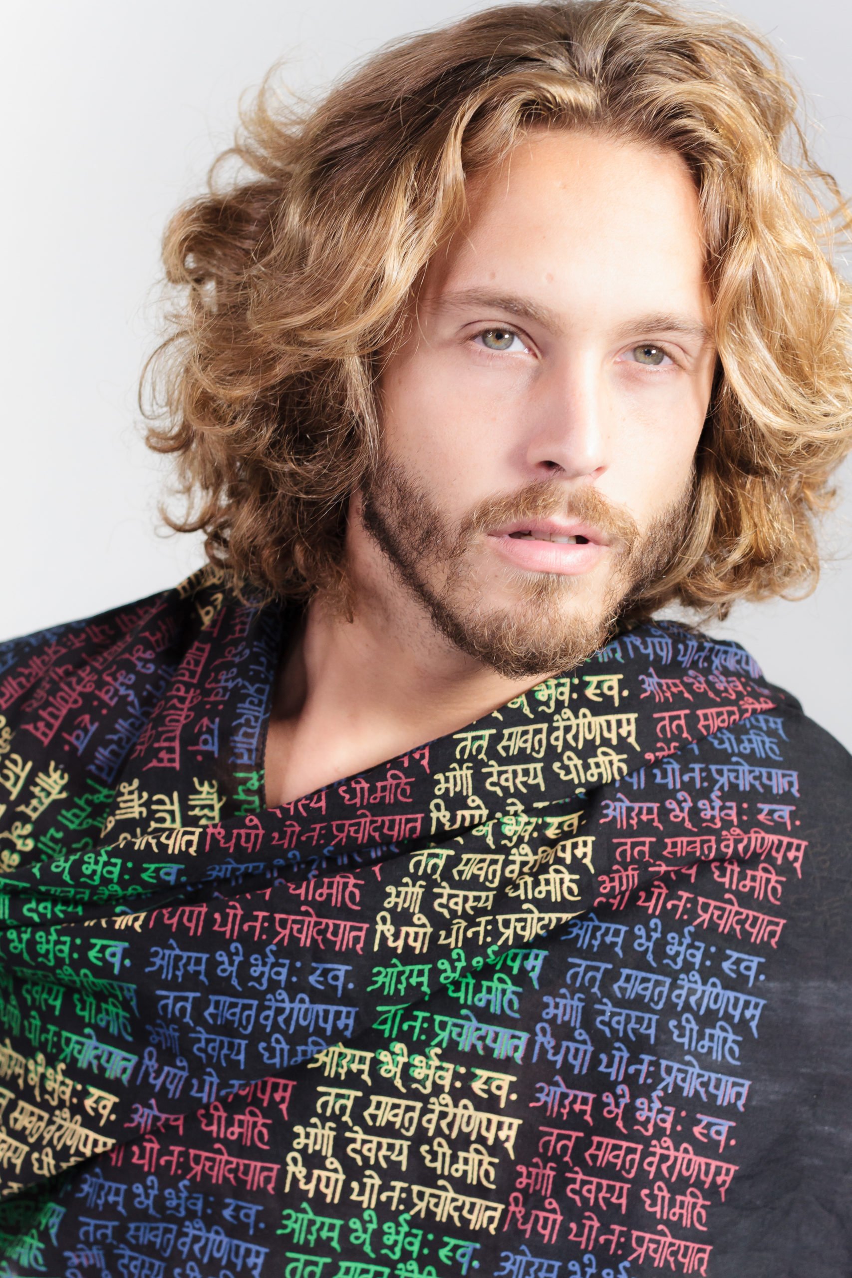 a male model wrapped in a black meditation scarf with contrastin gayatri mantra printed in primary colours