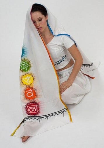 a seated model meditating with a hand painted chakra meditation wrap draped over her showing the vibrant painted chakra symbols