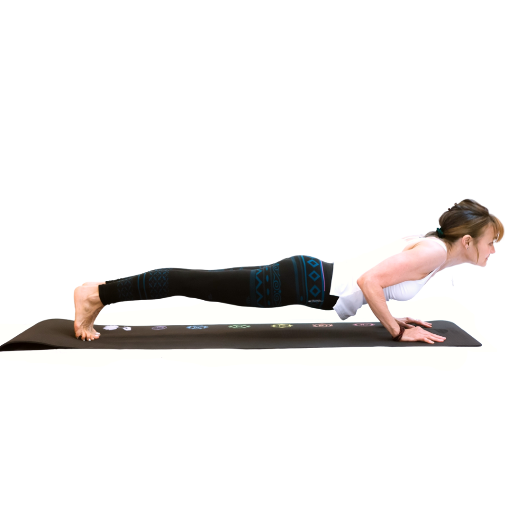 A lean yoga teacher performing chaturanga dandasana pose. She is stretched on a yoga mat supporting herself with her elbows at a right angle and the tips of her toes.  The pose is a low plank. She is wearing blue and black leggings in a geometric pattern and a white camisole top